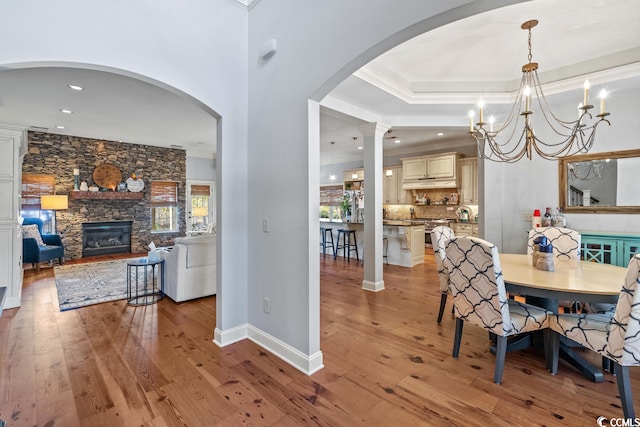 dining room with light wood-type flooring, a fireplace, crown molding, and a notable chandelier