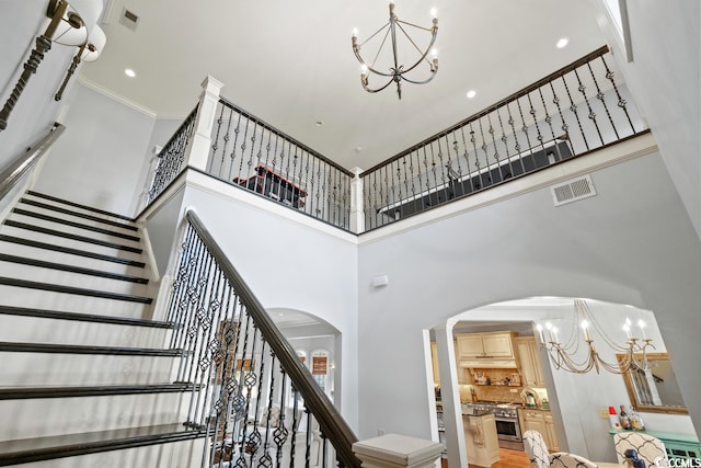 staircase featuring hardwood / wood-style floors, a chandelier, crown molding, and a towering ceiling