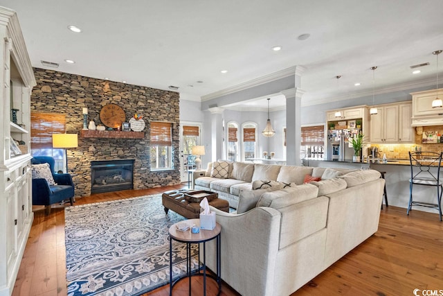 living room featuring ornate columns, ornamental molding, light wood-type flooring, and a fireplace