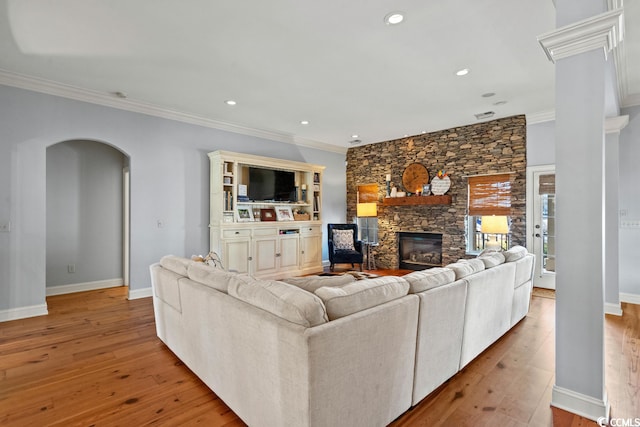 living room featuring crown molding, light hardwood / wood-style flooring, and a stone fireplace