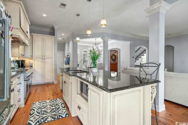 kitchen with a center island with sink, pendant lighting, decorative columns, stainless steel appliances, and light wood-type flooring