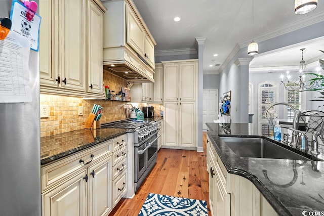 kitchen featuring ornamental molding, stainless steel appliances, sink, cream cabinets, and hanging light fixtures