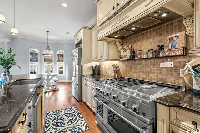 kitchen with light wood-type flooring, dark stone counters, custom exhaust hood, stainless steel appliances, and hanging light fixtures