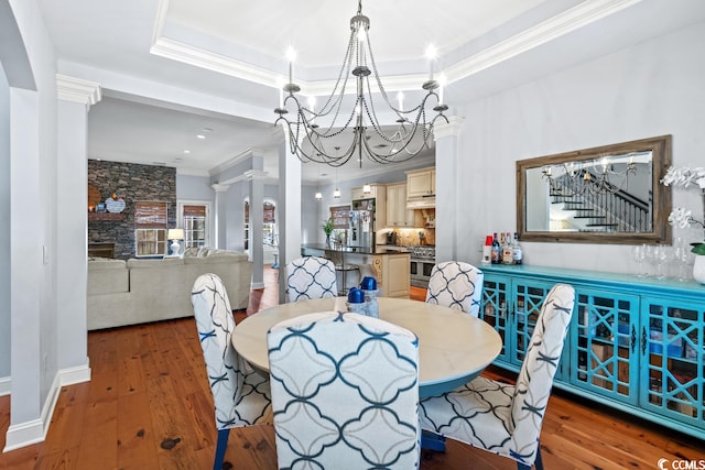 dining room with hardwood / wood-style flooring, a raised ceiling, an inviting chandelier, and ornate columns