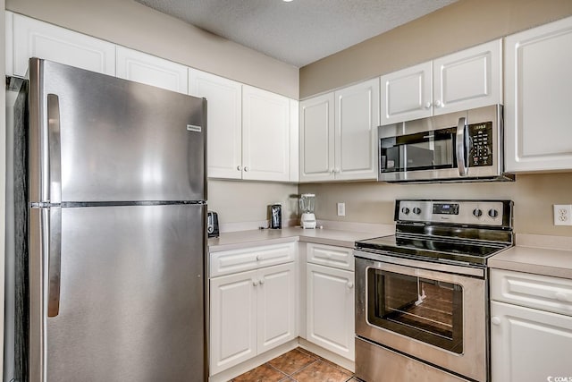 kitchen with dark tile patterned flooring, a textured ceiling, stainless steel appliances, and white cabinetry