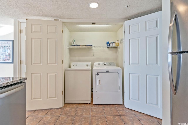 clothes washing area with light tile patterned floors, washer and dryer, and a textured ceiling