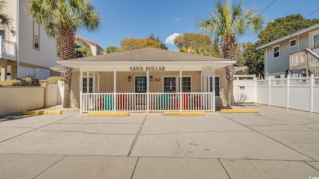 view of front facade featuring a shingled roof, fence, and a porch