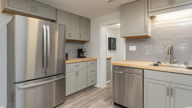 kitchen with wooden counters, sink, light hardwood / wood-style flooring, decorative backsplash, and stainless steel appliances