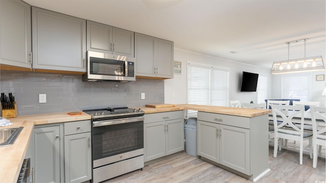 kitchen with kitchen peninsula, light wood-type flooring, stainless steel appliances, pendant lighting, and gray cabinets