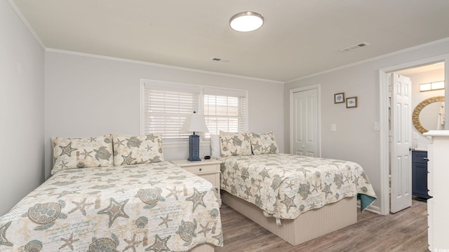 bedroom with a closet, wood finished floors, visible vents, and crown molding