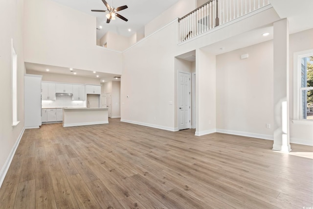 unfurnished living room with baseboards, a ceiling fan, a high ceiling, light wood-style floors, and recessed lighting