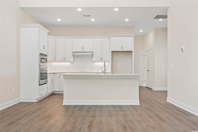 kitchen with under cabinet range hood, a kitchen island with sink, visible vents, and white cabinets