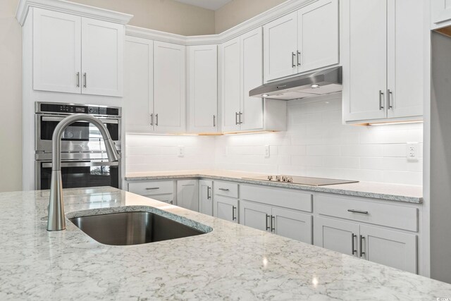 kitchen with tasteful backsplash, light stone counters, stainless steel double oven, black electric cooktop, and white cabinets