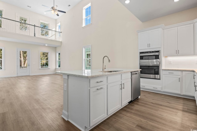 kitchen featuring light wood finished floors, appliances with stainless steel finishes, open floor plan, white cabinetry, and a sink