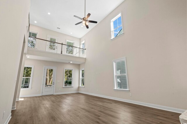 unfurnished living room with ceiling fan, dark wood-type flooring, and a high ceiling