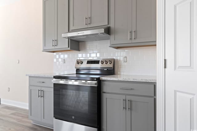 kitchen with light hardwood / wood-style flooring, gray cabinetry, stainless steel range with electric cooktop, light stone countertops, and decorative backsplash