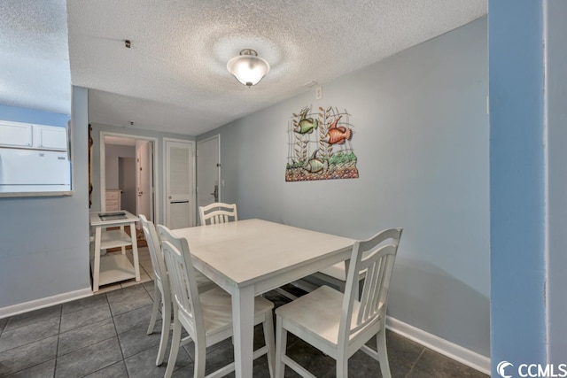 dining room featuring a textured ceiling, dark tile patterned flooring, and baseboards