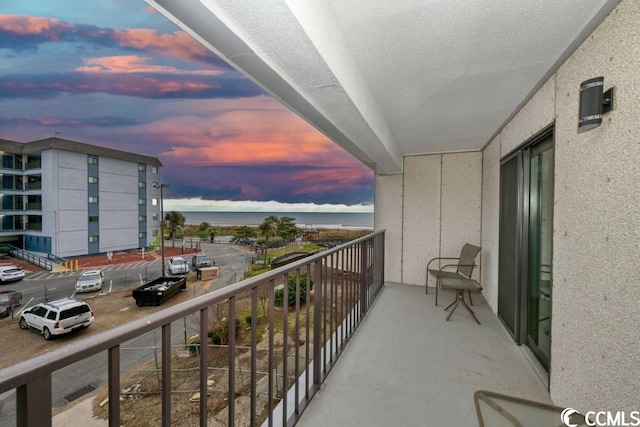 balcony at dusk featuring a water view