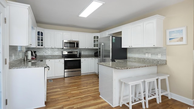 kitchen featuring a peninsula, appliances with stainless steel finishes, glass insert cabinets, and a sink