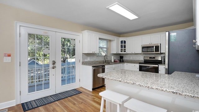 kitchen featuring light stone counters, a peninsula, white cabinets, appliances with stainless steel finishes, and light wood-type flooring