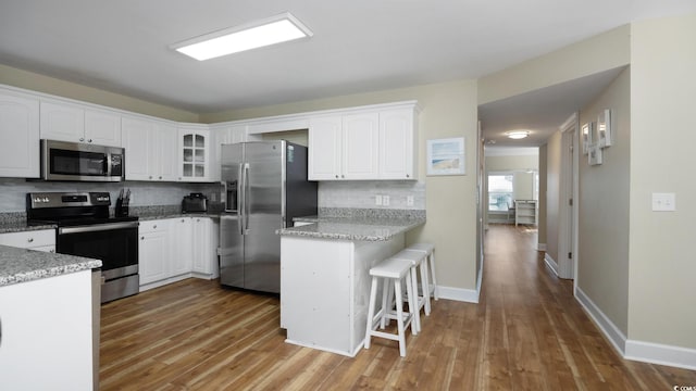 kitchen featuring wood finished floors, appliances with stainless steel finishes, a breakfast bar, and white cabinetry