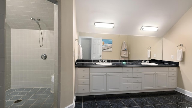 bathroom featuring a tile shower, double vanity, a sink, and baseboards