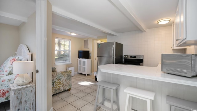 kitchen with light tile patterned floors, a kitchen breakfast bar, beamed ceiling, a peninsula, and stainless steel appliances