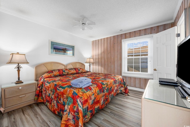 bedroom with wooden walls, ceiling fan, ornamental molding, light hardwood / wood-style floors, and a textured ceiling