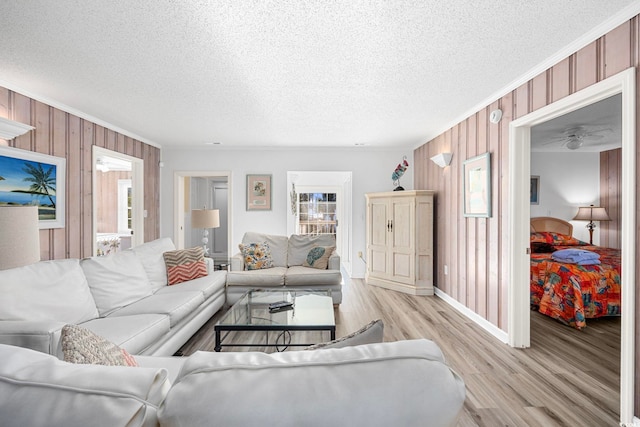 living room featuring light wood-type flooring, wood walls, and a textured ceiling