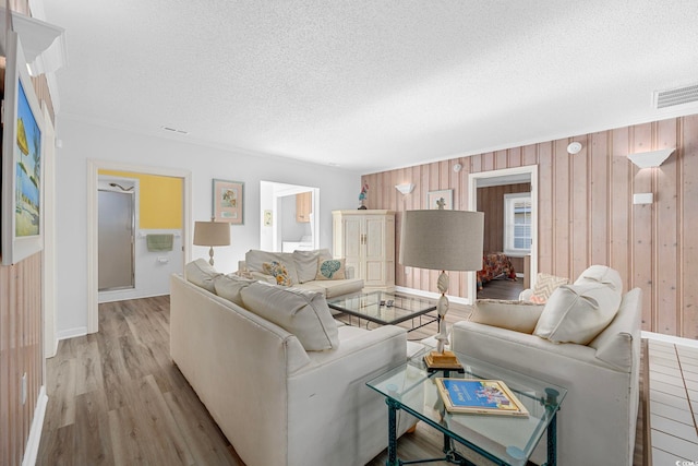 living room featuring light hardwood / wood-style flooring, wood walls, and a textured ceiling