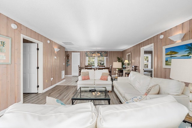 living room with a notable chandelier, wooden walls, and light hardwood / wood-style flooring