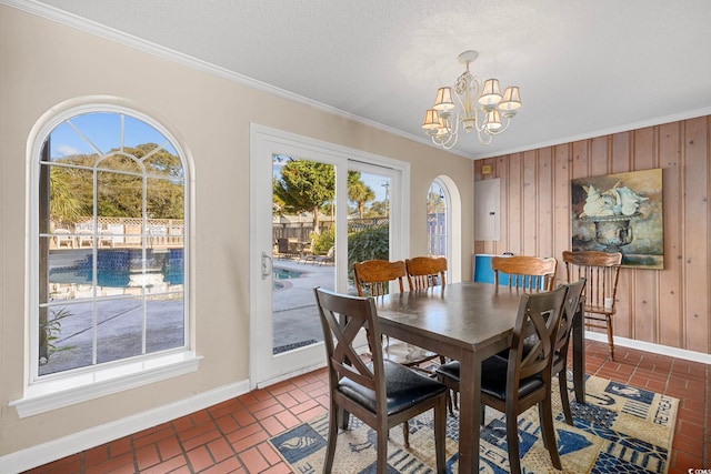 dining room featuring an inviting chandelier, ornamental molding, wood walls, and a textured ceiling