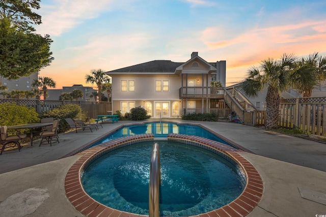 pool at dusk featuring an in ground hot tub and a patio area