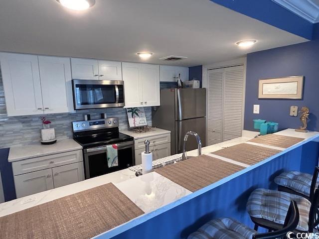 kitchen with a kitchen breakfast bar, stainless steel appliances, white cabinetry, and tasteful backsplash