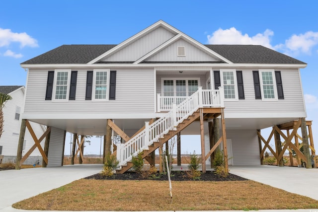 raised beach house featuring driveway, covered porch, a shingled roof, and a carport