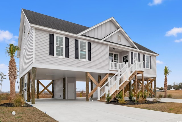 coastal home featuring concrete driveway, stairway, roof with shingles, covered porch, and a carport