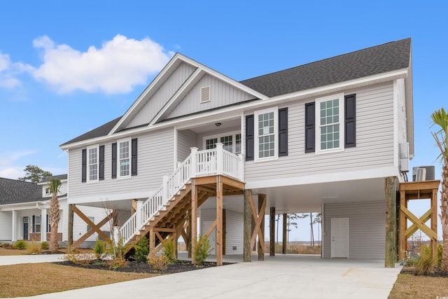 coastal inspired home with a shingled roof, concrete driveway, board and batten siding, a carport, and stairs