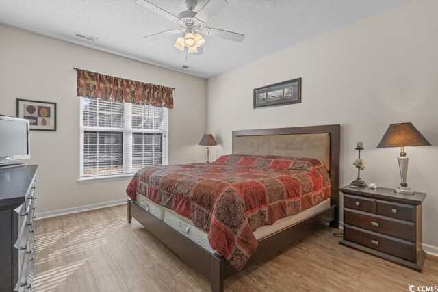 bedroom with light wood finished floors, baseboards, visible vents, ceiling fan, and a textured ceiling