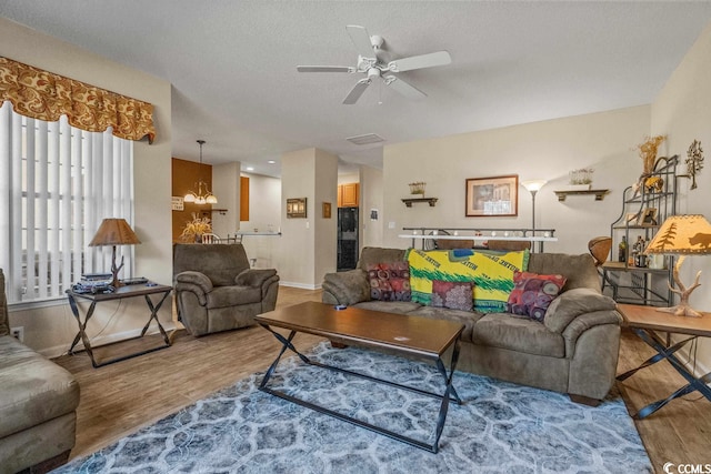 living area with a textured ceiling, baseboards, wood finished floors, and ceiling fan with notable chandelier