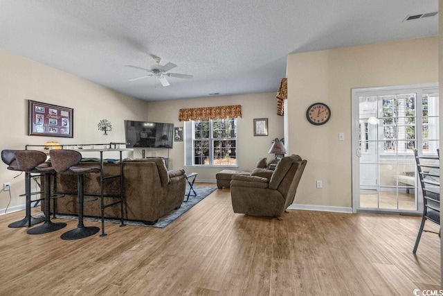 living room featuring baseboards, a textured ceiling, a ceiling fan, and wood finished floors