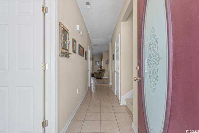 corridor with baseboards, light tile patterned flooring, visible vents, and a textured ceiling