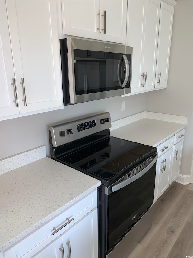 kitchen featuring light stone counters, white cabinets, appliances with stainless steel finishes, and light hardwood / wood-style flooring