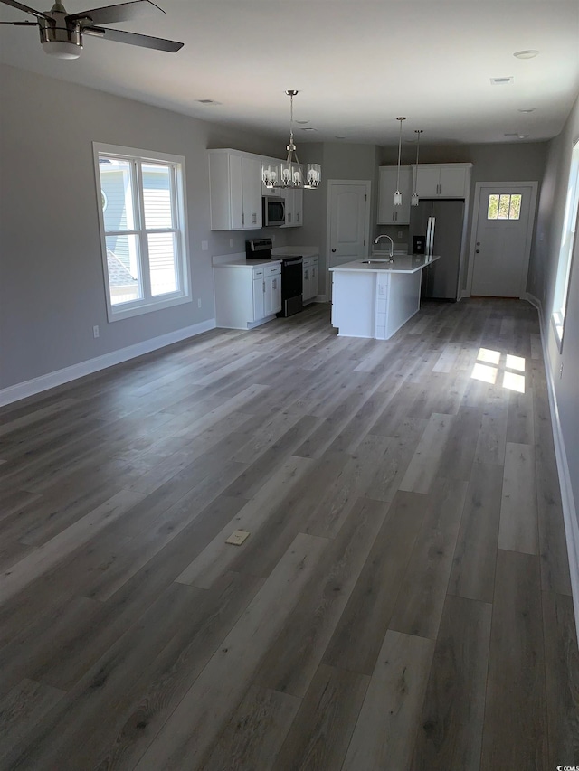 kitchen featuring an island with sink, decorative light fixtures, ceiling fan with notable chandelier, hardwood / wood-style floors, and appliances with stainless steel finishes