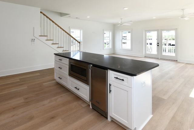 kitchen with white cabinetry, stainless steel microwave, ceiling fan, and light wood-type flooring