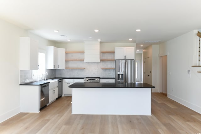 kitchen with a kitchen island, white cabinets, backsplash, stainless steel appliances, and light hardwood / wood-style flooring