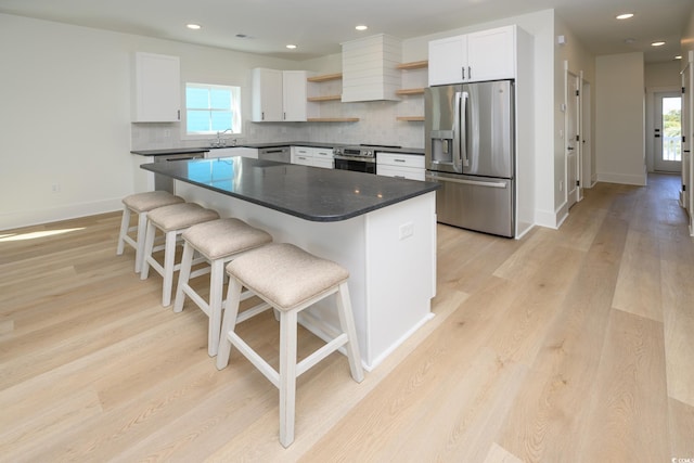 kitchen with open shelves, stainless steel fridge, dark countertops, and plenty of natural light