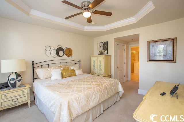 carpeted bedroom featuring a tray ceiling, ornamental molding, ensuite bath, and ceiling fan