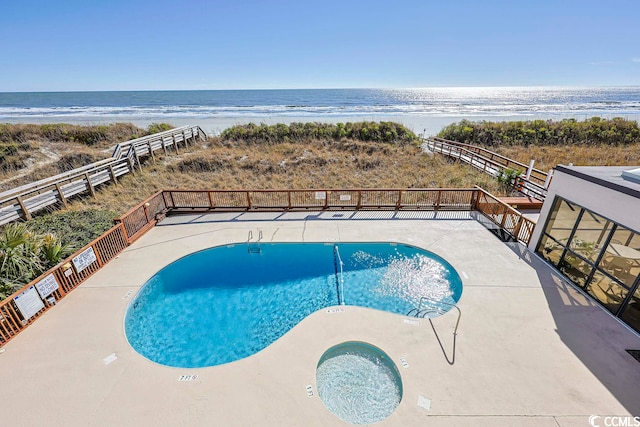 view of pool with a community hot tub, a water view, and a view of the beach