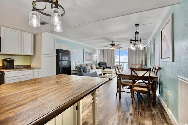 kitchen with white cabinets, black refrigerator, hanging light fixtures, and wooden counters