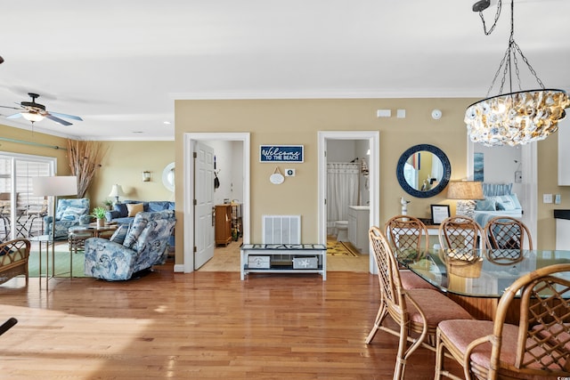 dining room with light hardwood / wood-style floors, ceiling fan with notable chandelier, and crown molding